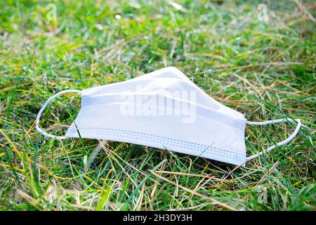 Nahaufnahme einer gebrauchten chirurgischen Gesichtsmaske, die auf dem Gras liegt. Einwegmasken, die Schadstoffrisiken für die Umwelt Bergen. Stockfoto