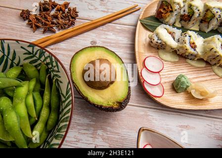 Japanische Gerichte mit Avocado, Uramaki california Roll Sushi, Pod edamame, Sternanis, Radieschscheiben, Wasabi und Ginseng Stockfoto