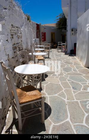 Sikinos Island, Griechenland schmale Gasse im alten DorfTaverna Tische und Stühle auf einer Terrasse Vertikale Aufnahme Stockfoto