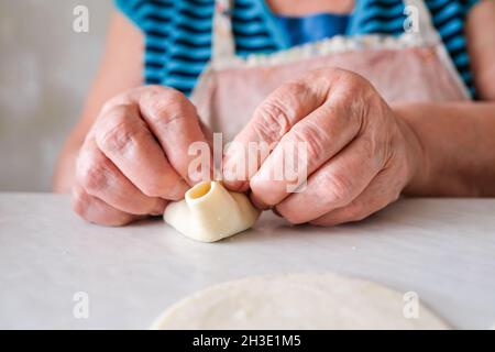 Hände und Teig. Alte Frau formt Pasta. Oma macht Manti. Rezept für Fleisch und Teig. Stockfoto