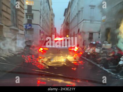 Regen auf der Straße mit Farbbeleuchtung an einem Verkehrsabend, Blick vom Auto auf der Straße, wenn es Regenzeit in der Stadt Wetter. Stockfoto