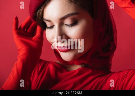 Nahaufnahme einer lächelnden jungen Frau, die die Baskenmütze auf Rot anpasst Stockfoto