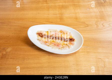 Spanische Borriquete Fisch Sashimi mit Olivenöl und Pfeffer auf weißem Teller und Holztisch Stockfoto