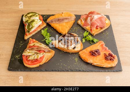 Verschiedene Toast mit norwegischem Lachs, Käse mit Ratatouille, Creme mit Sardellen, iberischer Schinken, Ziegenkäse mit Pilzen, serviert in einer spanischen Tapas-r Stockfoto