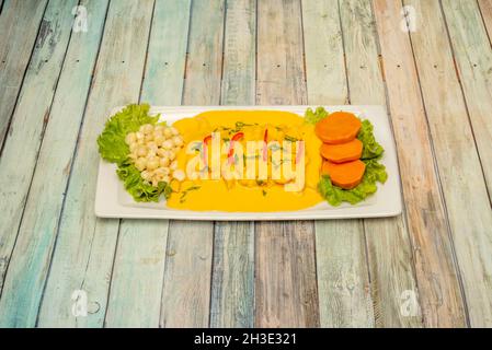 Peruanisches Fischrezept tiradito mit gekochtem Mais, viel gelber Sauce und Scheiben Süßkartoffeln auf einem weißen Tablett Stockfoto