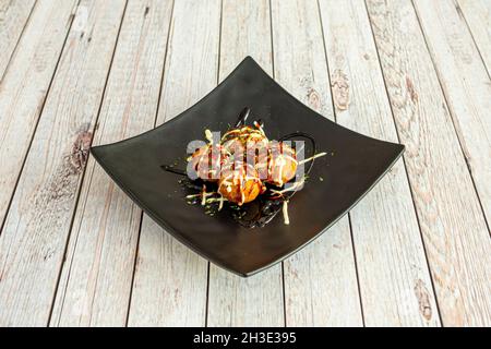 Tablett mit japanischem Oktopus Takoyaki, zerschlagen mit Sojasauce und Schnittlauch mit Petersilie Stockfoto