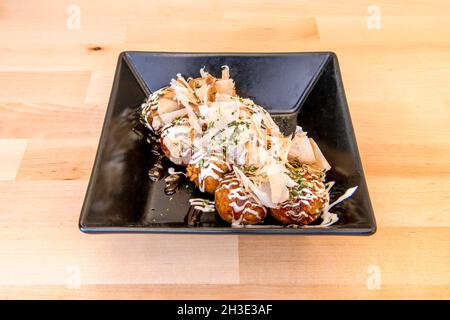 Schwarzer Teller mit japanischem Oktopus Takoyaki und Scheiben getrockneten Thunfisch mit Saucen und Schnittlauch Stockfoto