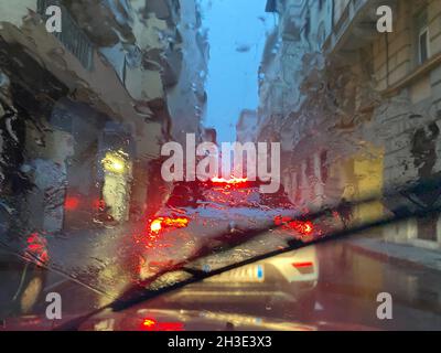 Regen auf der Straße mit Farbbeleuchtung an einem Verkehrsabend, Blick vom Auto auf der Straße, wenn es Regenzeit in der Stadt Wetter. Stockfoto