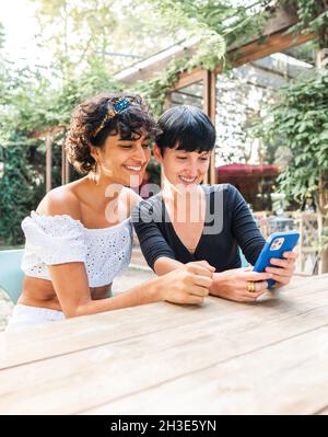 Content-freundliche, multirassische Frauen, die auf dem Handy surfen, während sie das Wochenende gemeinsam im Sommerpark genießen Stockfoto