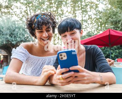 Content-freundliche, multirassische Frauen, die auf dem Handy surfen, während sie das Wochenende gemeinsam im Sommerpark genießen Stockfoto