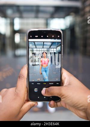 Crop anonyme Person, die Foto von afroamerikanischen Frau in stilvoller Kleidung auf dem Smartphone, während auf der Straße vor verschwommenem Hintergrund stehen Stockfoto