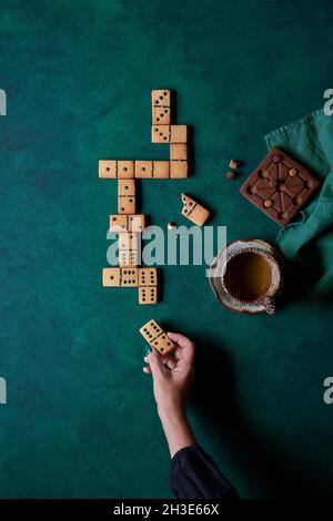 Draufsicht auf Ernte anonyme Person essen süßen Domino geformten Cookies und trinken heißen Kaffee auf grünem Hintergrund Stockfoto