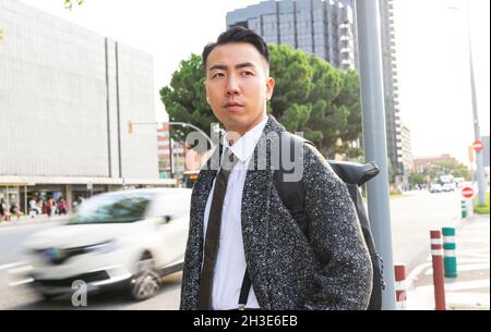 Selbstbewusster junger asiatischer Unternehmer in stilvoller Kleidung, der in der sonnigen Stadt absieht Stockfoto