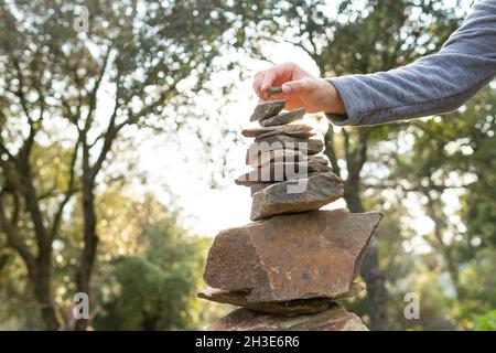 Niedriger Erntewinkel nicht erkennbarer männlicher Reisender stapelt Steine während des Trekkings in üppig grünen Wäldern an sonnigen Tagen Stockfoto