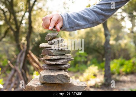 Ernte unerkennbare männliche Reisende stapeln Steine während Trekking in üppig grünen Wald an sonnigen Tag Stockfoto