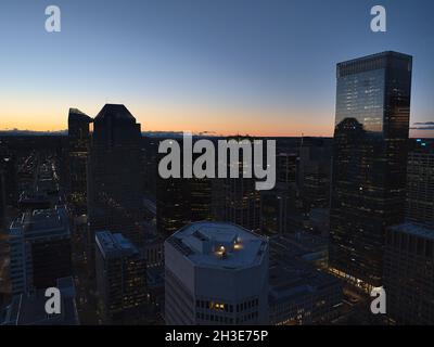 Atemberaubende Luftaufnahme der westlichen Innenstadt von Calgary nach Sonnenuntergang mit den Silhouetten von beleuchteten Wolkenkratzern und dem orangefarbenen Himmel am Horizont. Stockfoto