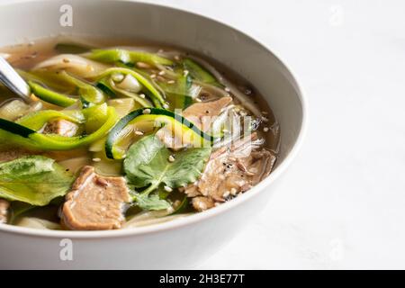 Schüssel mit traditioneller vietnamesischer Nudelsuppe Pho bo mit Basilikumblättern und Kalk auf Marmortisch im hellen Raum Stockfoto