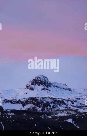 Malerische Landschaft aus felsigen Bergen mit schneebedeckten Gipfeln vor dem atemberaubenden rosa Sonnenuntergangshimmel in Island Stockfoto
