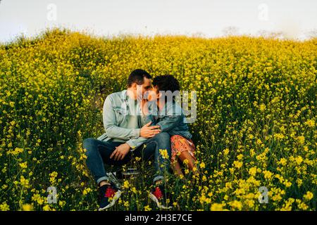 Liebevolles junges multirassisches Paar in lässiger Kleidung, das während eines romantischen Datums am sonnigen Tag in üppiger blühender Wiese küsst Stockfoto
