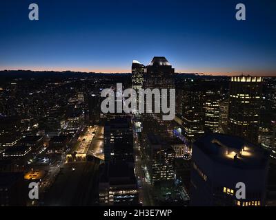 Atemberaubende Luftaufnahme der westlichen Innenstadt von Calgary mit beleuchteten Bürogebäuden nach Sonnenuntergang und orangefarbenem Himmel am Horizont in der Herbstsaison. Stockfoto