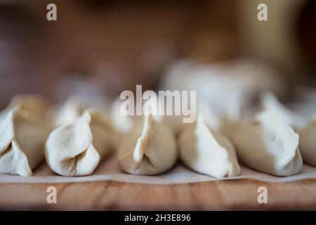 Nahaufnahme von gefüllten, ungekochten Jiaozi-Knödeln, serviert auf einem Holztisch in der Küche Stockfoto