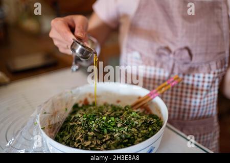 Von oben der Ernte unkenntlich Hausfrau in Schürze Gießen Olivenöl in Schüssel mit rohem Hackfleisch und Kräutern während der Vorbereitung Füllung für Jiaozi du Stockfoto