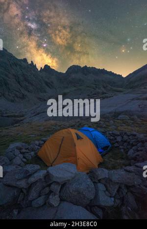 Panoramablick auf das Zelt am Seeufer gegen verschneite Berge unter dem wolkigen milchigen Himmel am Abend im Circo de Gredos cirque in Spanien Stockfoto