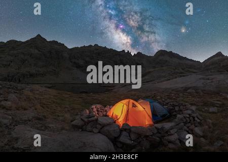 Panoramablick auf das Zelt am Seeufer gegen verschneite Berge unter dem wolkigen milchigen Himmel am Abend im Circo de Gredos cirque in Spanien Stockfoto