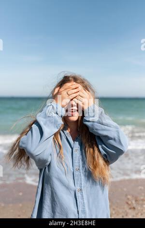 Junge Weibchen bedecken das Gesicht mit Händen, während sie an sonnigen Sommertagen an der Küste stehen Stockfoto