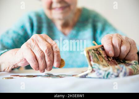 Detailliertes Nahaufnahme-Foto von älteren 96-jährigen Frauenhänden, die nach der Bezahlung von Rechnungen die verbleibenden Rentenmünzen in ihrem Portemonnaie zählen. Die Untragbarkeit der Sozialtransfers und des Rentensystems. | Modellgenehmigung verfügbar Stockfoto