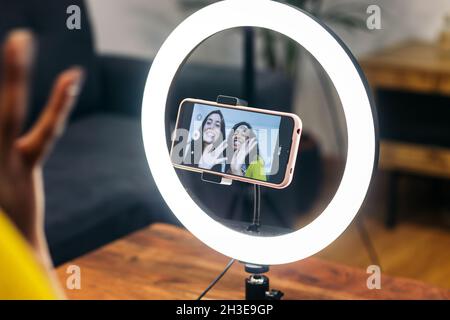 Crop anonyme Person mit modernen Smartphone mit Beleuchtung Ringlampe auf Stativ für das Anrufen von Freunden Stockfoto