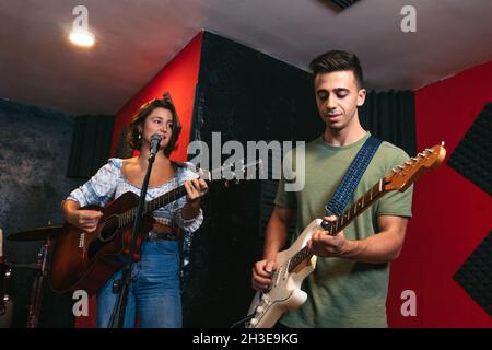 Positiver junger Mann, der Gitarre spielt, neben einer Musikerin, die akustische Gitarre spielt und im Lichtclub singt Stockfoto