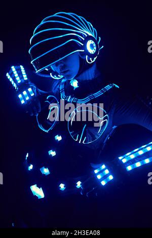 Gesichtslose Person in zeitgenössisch glühender Cyborg-Anzug mit Neonbeleuchtung und Helm auf schwarzem Hintergrund in dunklem Studio Stockfoto