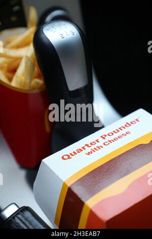 Ein McDonald's-Menü im Auto. Hier pommes frites und ein Hamburger mit einem Viertel Pounder am Schalthebel. Stockfoto