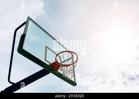 Von unten Basketballkorb mit Netz und Backboard auf Sportplatz gegen blauen Himmel mit Wolken am sonnigen Tag platziert Stockfoto