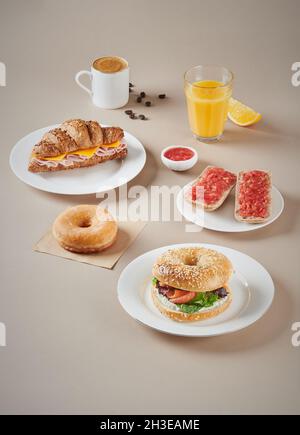 Sandwiches mit Fleisch und Croissant auf Tellern und Bagels, die in der Nähe eines Glases Orangensaft und einer Tasse Kaffee platziert werden Stockfoto