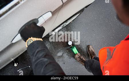 Nahaufnahme der automatischen Notbeine mit Luftkompressor, die den Platten Reifen aufblasen. Mann, der den Reifen mit einem Luftkompressor aufbläst, während er auf einer verregneten Straße neben dem Auto steht. Konzept des Notdienstes im Straßenverkehr. Stockfoto