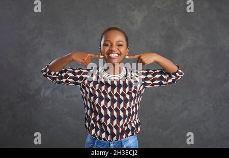 Porträt einer glücklichen jungen schwarzen Frau, die mit perfekten weißen Zähnen auf ihr Lächeln zeigt Stockfoto