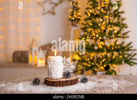 Selektiver Fokus auf das Kerzenbrennen von Schneeballmustern, dekoriert mit Pinienholzscheibe, weißer Schneeflocke-Dekoration und Kunstschnee auf dem Tisch. Stockfoto