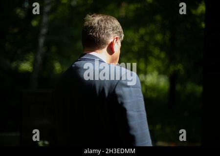 Eine Nahaufnahme eines Mannes an einem sonnigen Tag, ein Blick von hinten. Ein Mann in einem strengen blauen Anzug und einem weißen Hemd. Spaziergang im Park Stockfoto