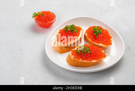 Sandwiches mit rotem Kaviar und frischen Kräutern auf grauem Hintergrund. Seitenansicht, Kopierbereich. Stockfoto