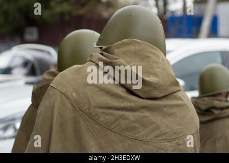 Drei Männer in sowjetischer Uniform während des Zweiten Weltkriegs, Blick von hinten. Grüner Mantel und Helm. Tag Des Sieges. Lifestyle In Der Stadt Stockfoto