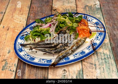 Traditioneller andalusischer Espeto aus Sardinen vom Holzkohlegrill mit grobem Meersalz und Salat aus Salat, Tomaten und roten Zwiebeln Stockfoto