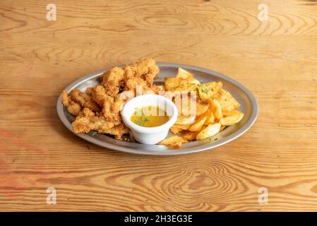 Tablett mit Hähnchenfingern im Teig mit Ei und Semmelbröseln, Petersilie, süßer, hausgemachter Sauce und hausgemachten Chips auf einem Metalltablett Stockfoto