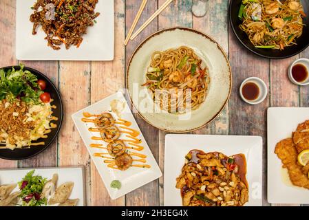 Stellen Sie sich udon-Nudeln mit Garnelen, Wok-sautiertem Gemüse, gedämpften Gyozas, karamellisierten Rinderstreifen mit Sojasauce, Huhn mit Nüssen aus der oberen Ansicht vor. Stockfoto