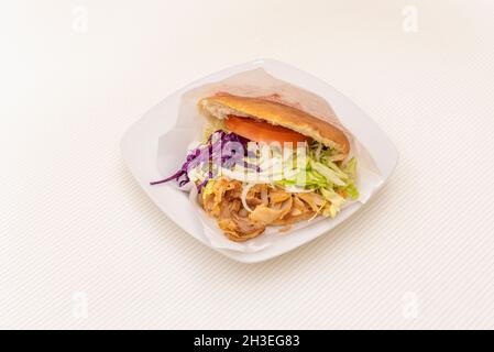 Gegrilltes Chicken Döner Kebab Sandwich mit Zwiebeln, purpurem Kohl, Salat und Tomaten mit Joghurt und Tomatensauce auf weißem Tisch Stockfoto