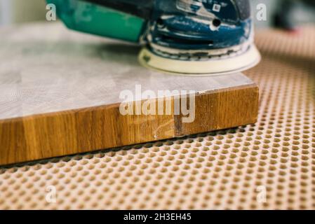 Der Zimmermann poliert in einer Werkstatt ein Holzbrett. Der Prozess der Schleifmaschine. Herstellung von Holzmöbeln. Schleifen von Teilen. Stockfoto