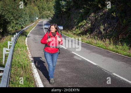 Eine Touristin, in einer Jacke, trampend auf der Straße, spaziert entlang der portugiesischen Forststraßen. Hält andere Reisende an. Stockfoto