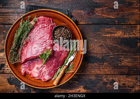 Zwei Lappen oder Flanken rohes Rindfleisch Steaks auf einem rustikalen Teller mit Kräutern. Dunkler Holzhintergrund. Draufsicht. Speicherplatz kopieren Stockfoto