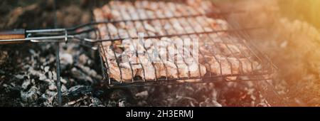 Grillen unter Campingbedingungen. Schweinefleisch wird auf dem Grill auf schwelenden Kohlen oder vom Lagerfeuer auf dem Boden im Sommer oder Herbst sogar gebraten Stockfoto